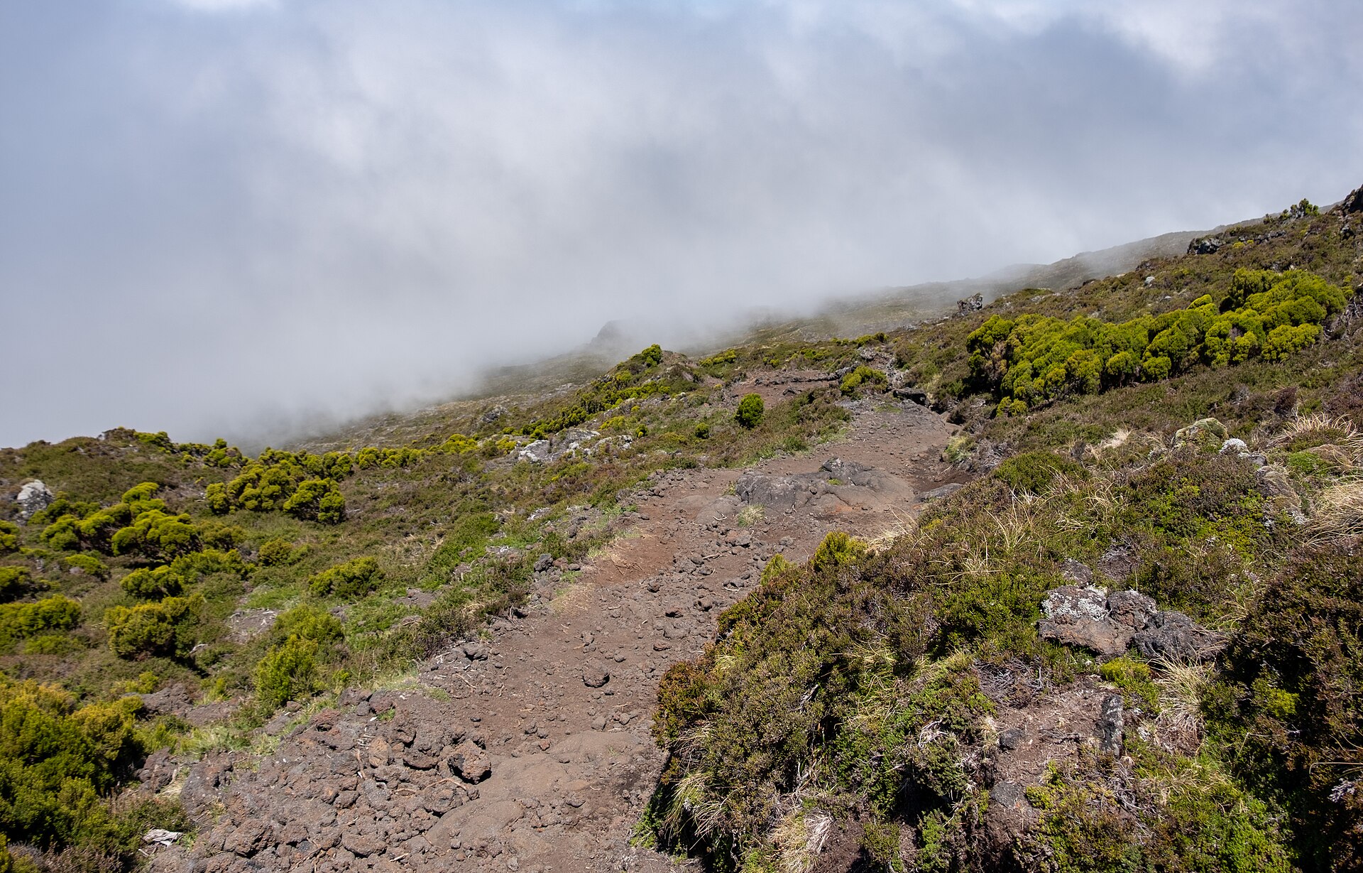 Walkers on the loose volcanic rock of the ascent route up Montanha do Pico
