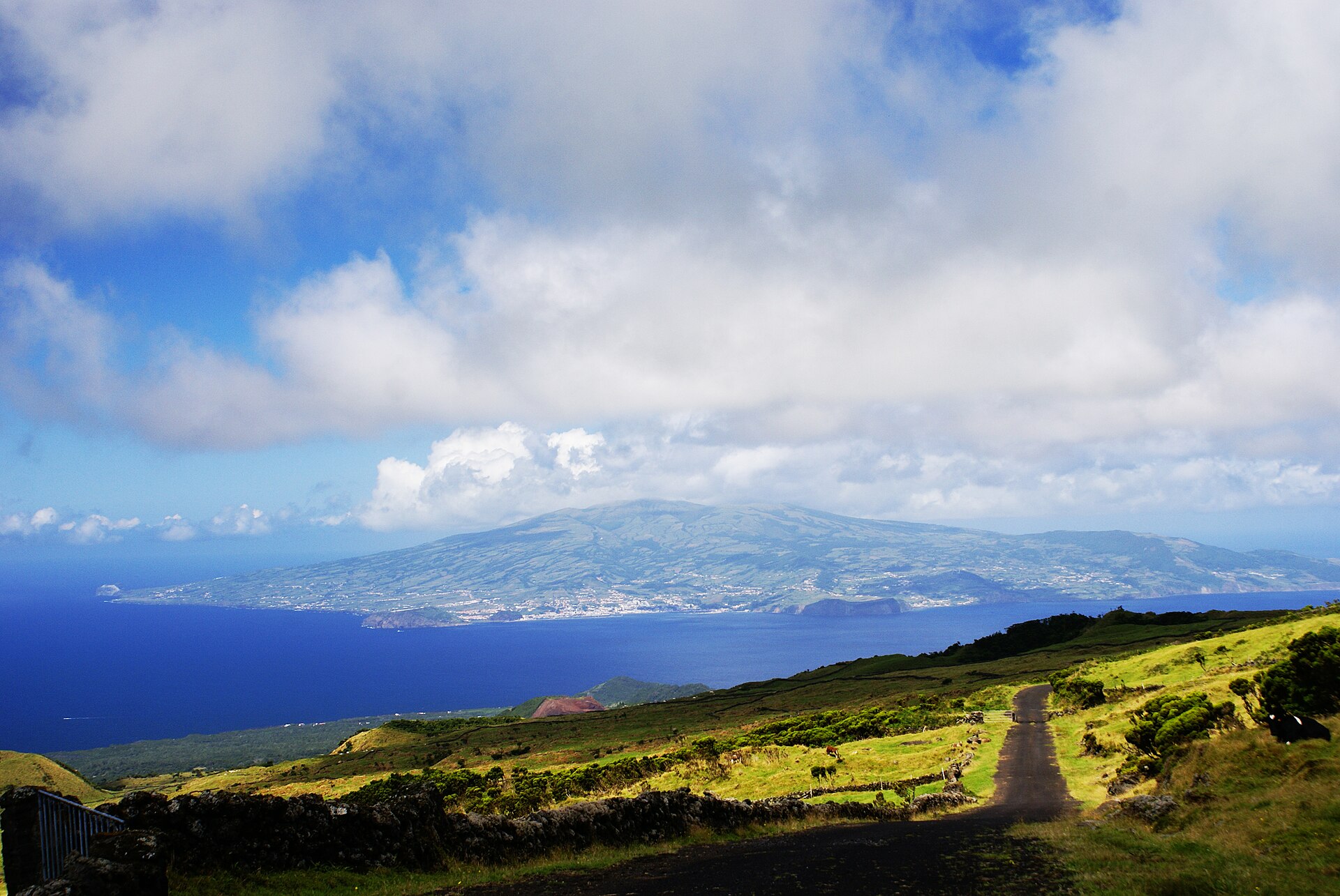 Green farmland across Pico's interior with Faial visible across the water beyond