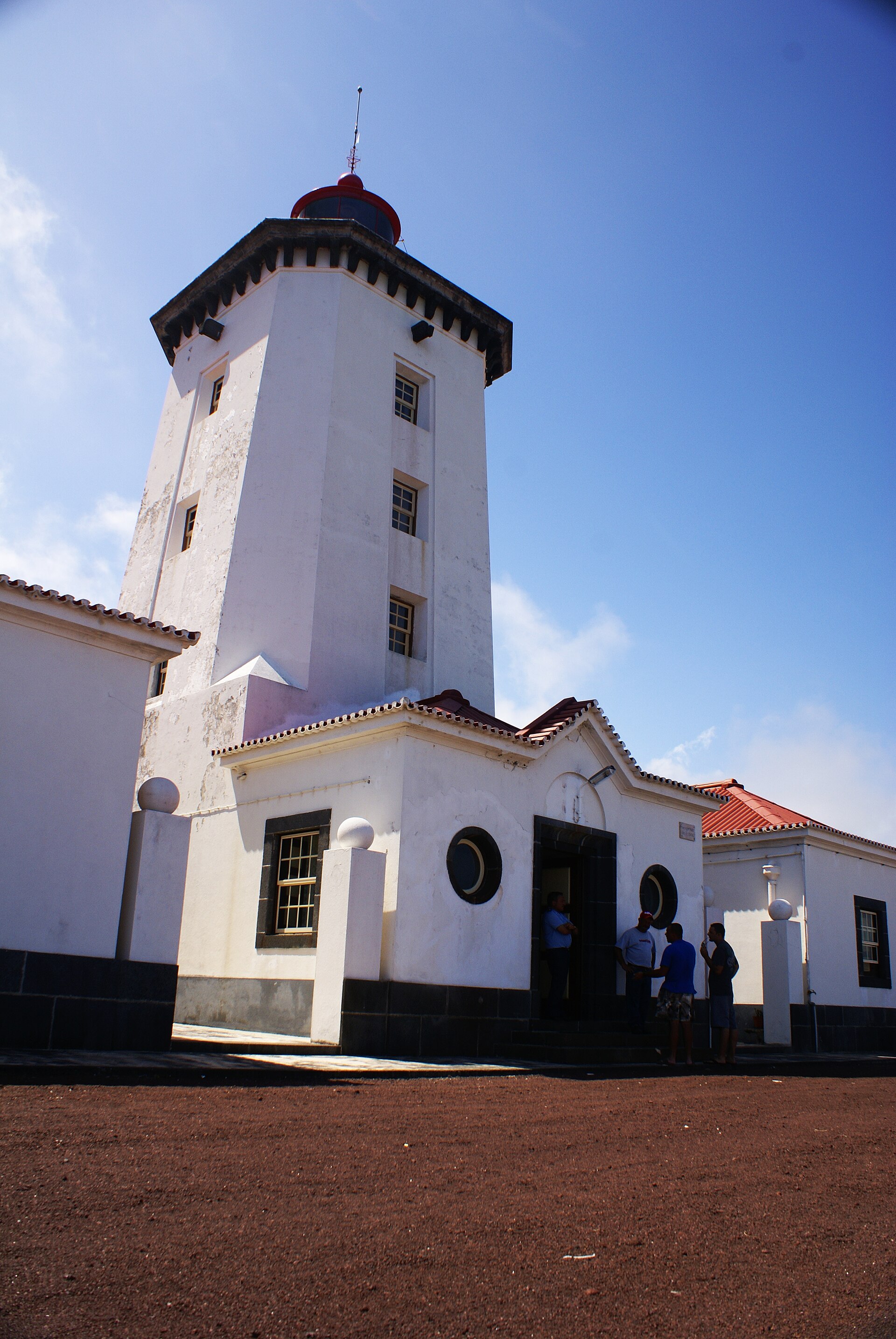 A white square lighthouse tower with a red lantern, above its single-storey keepers' buildings
